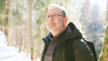 Outdoor portrait of middle age 55 - 60 year old man hiking in winter forest, wearing warm jacket and black backpack